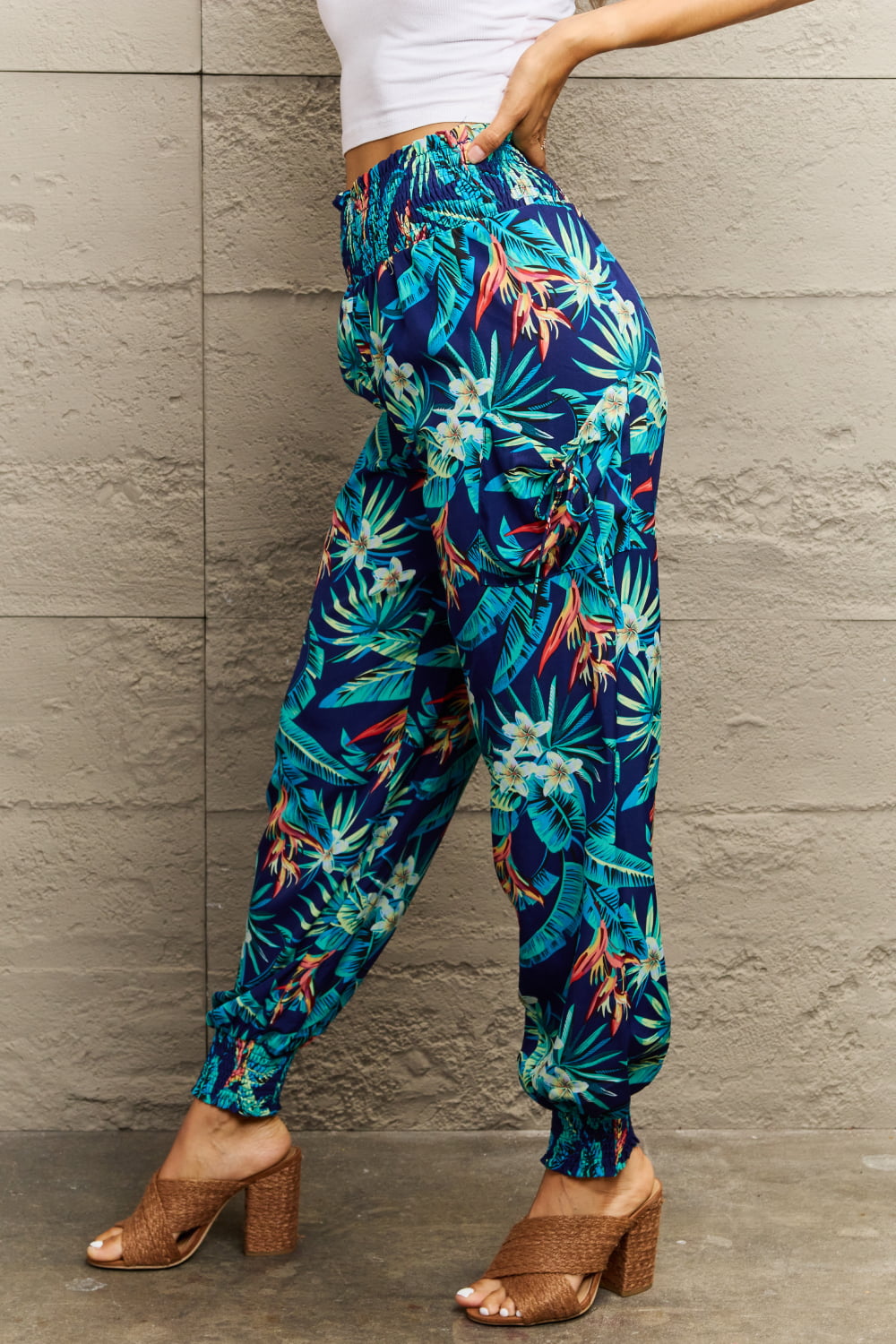 Person wearing tropical print pants and brown sandals against a gray wall.