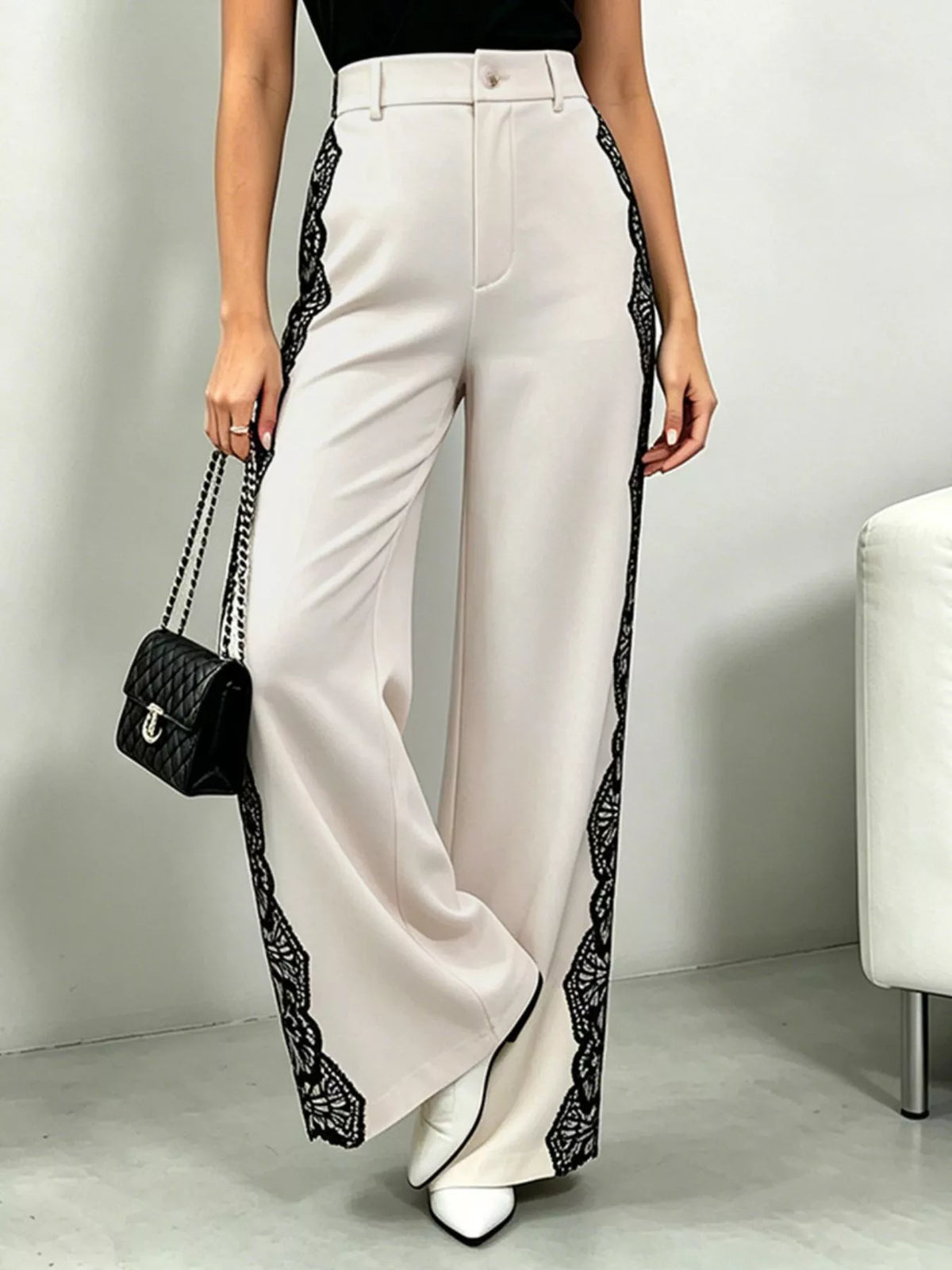 White pants with black lace trim worn by a person, holding a black handbag.