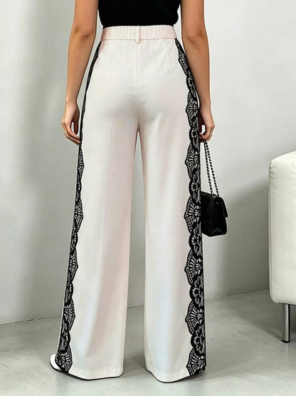 White pants with black lace trim worn by a person, standing against a plain background.