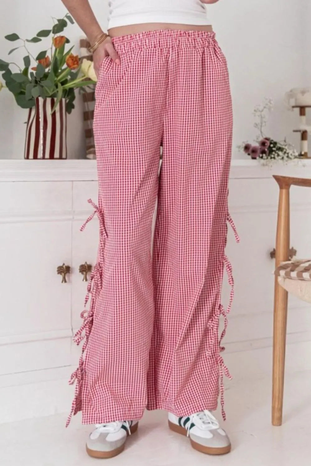 Person wearing red checkered pants with ruffles in a room with white cabinets and flowers.