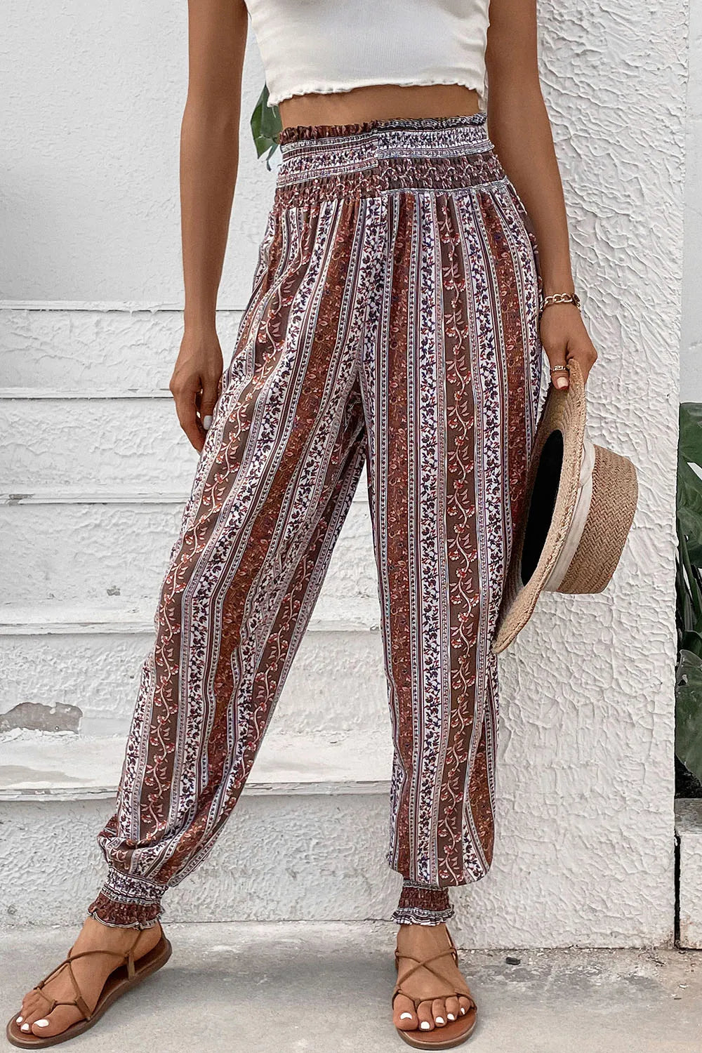 Person wearing patterned pants with a white top and straw hat against a textured wall.