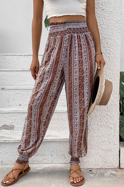 Person wearing patterned pants with a white top and straw hat against a textured wall.